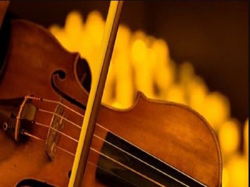 Close-up of a violin with a bow resting across its strings, warm amber stage lights in the background.