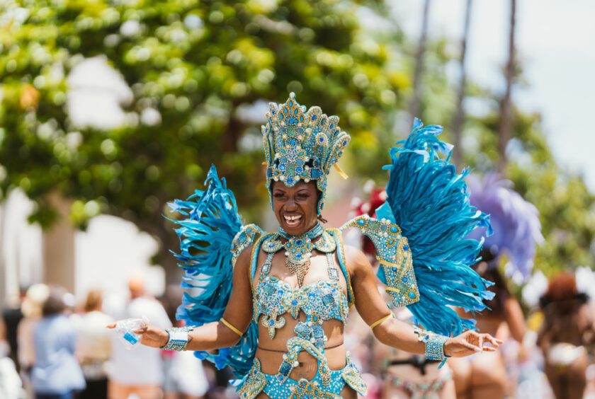 Dancer in a bright blue carnival costume with a jeweled headdress and large feather wings performing in a street parade.